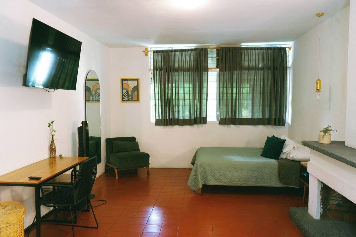 A room with a bed, a desk, a chair, a television, and a window with curtains.