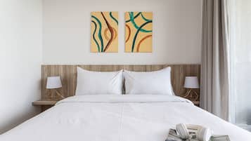 A hotel room with a large bed, two wall-mounted paintings, bedside lamps, and a window with curtains.