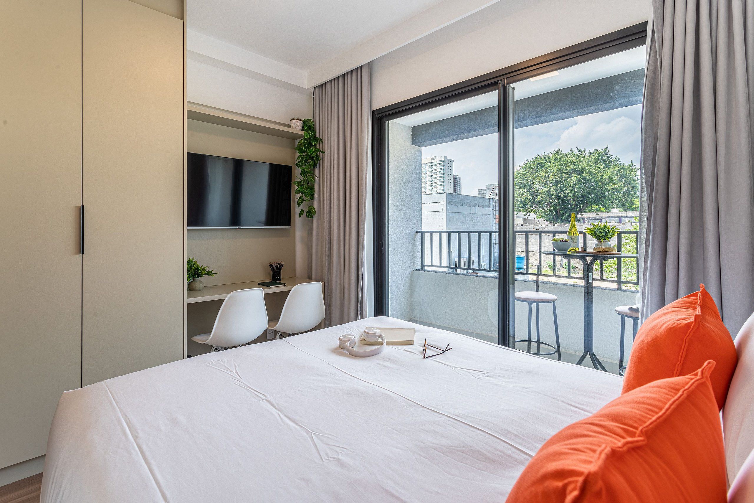 Une chambre d’hôtel moderne dotée d’un grand lit, d’un bureau avec deux chaises, d’une télévision et d’un balcon offrant une vue sur la ville.
