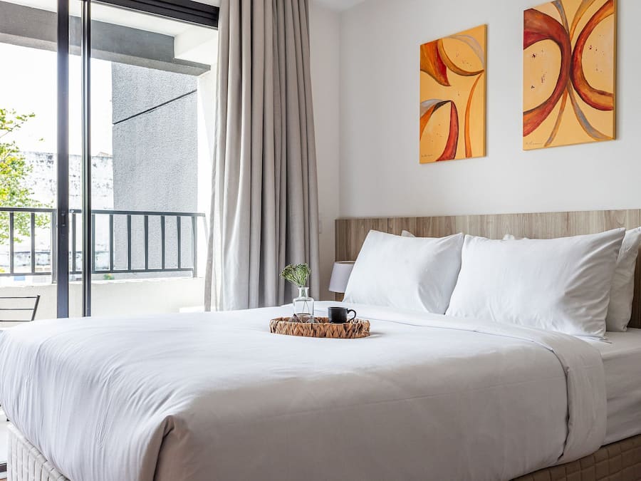 A hotel room with a bed, a window with curtains, a view of the outside, and two pieces of wall art.