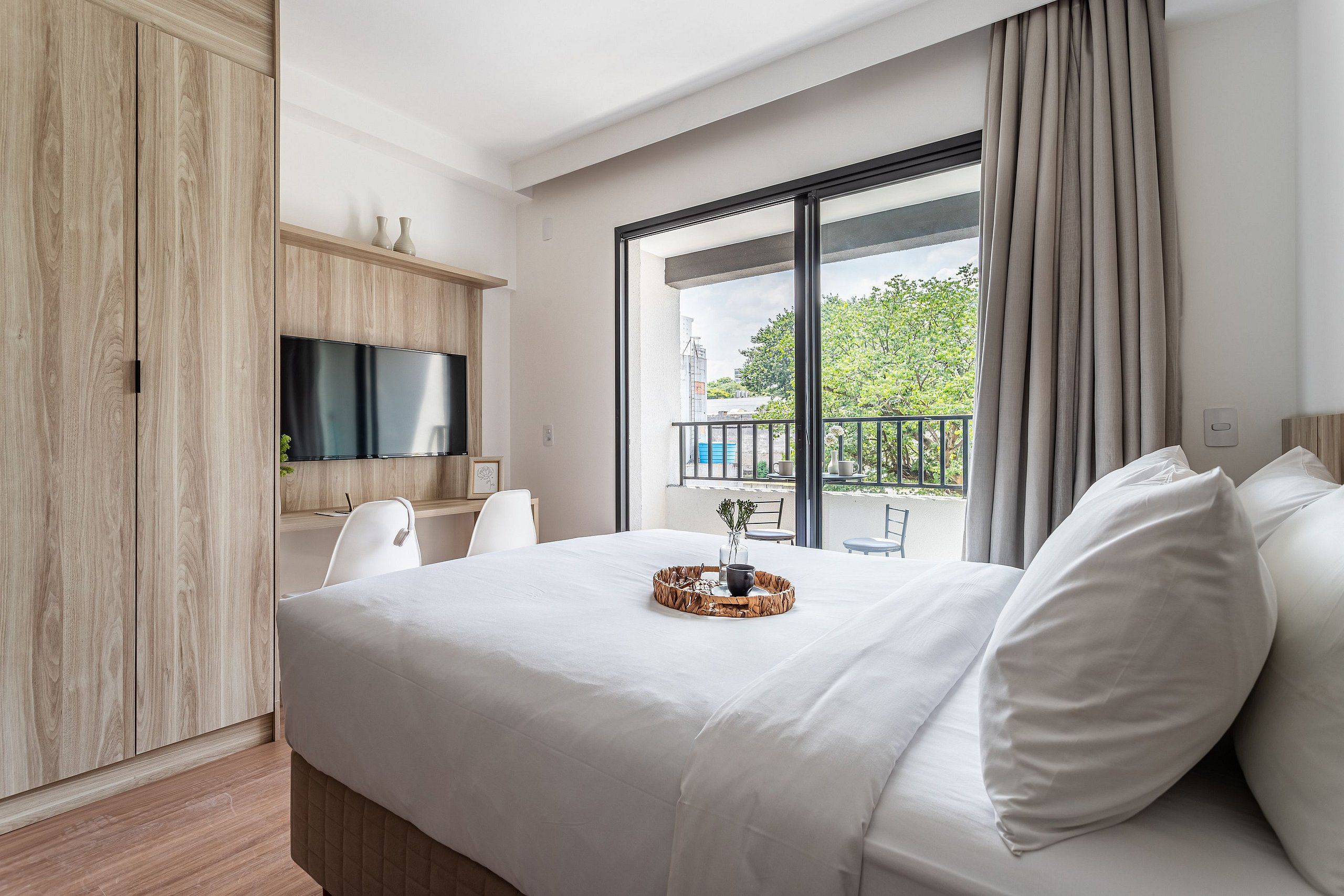Una habitación de hotel moderna con una cama grande, televisión, balcón con vistas y un armario de madera.