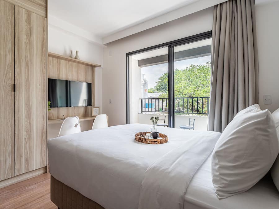 Quarto de hotel moderno com uma cama grande, televisão, varanda com vista e guarda-roupa de madeira.