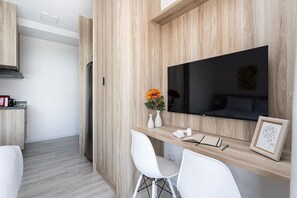 Una cocina moderna con un revestimiento de madera empotrado, un televisor de pantalla plana, una zona de comedor blanca con sillas y una pequeña mesa con adornos.