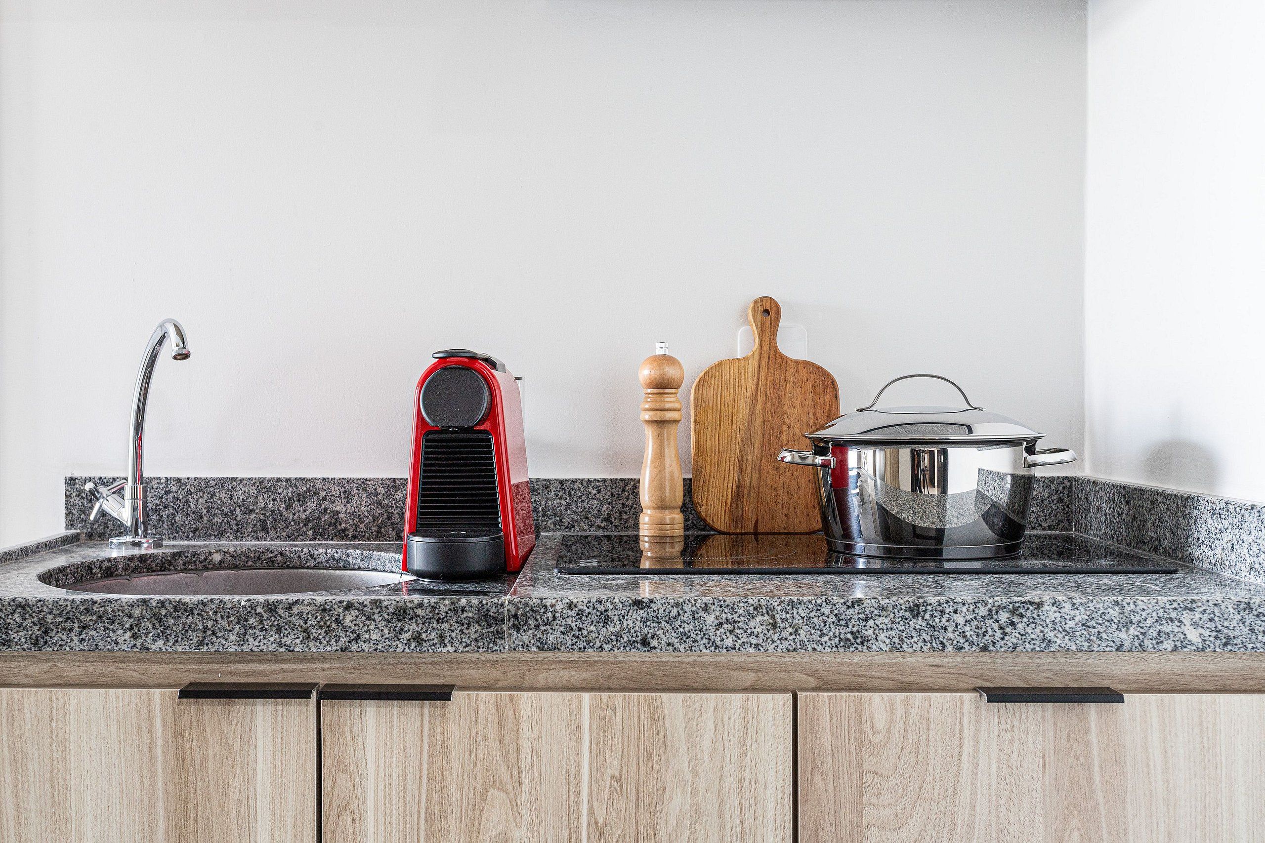 A kitchen with granite countertops, a stainless steel sink, a red appliance, a wooden cutting board, a pepper mill, and a pot on the stove.