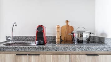 A kitchen with granite countertops, a stainless steel sink, a red appliance, a wooden cutting board, a pepper mill, and a pot on the stove.