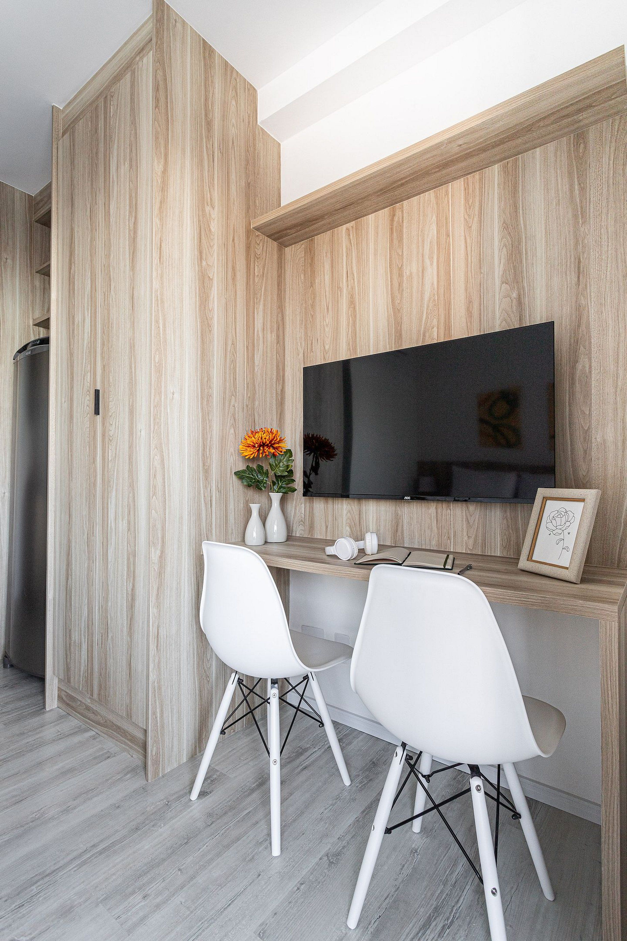 Een moderne eetruimte met een houten accentmuur, een flatscreen televisie, twee witte stoelen, een kleine tafel en een vaas met bloemen.