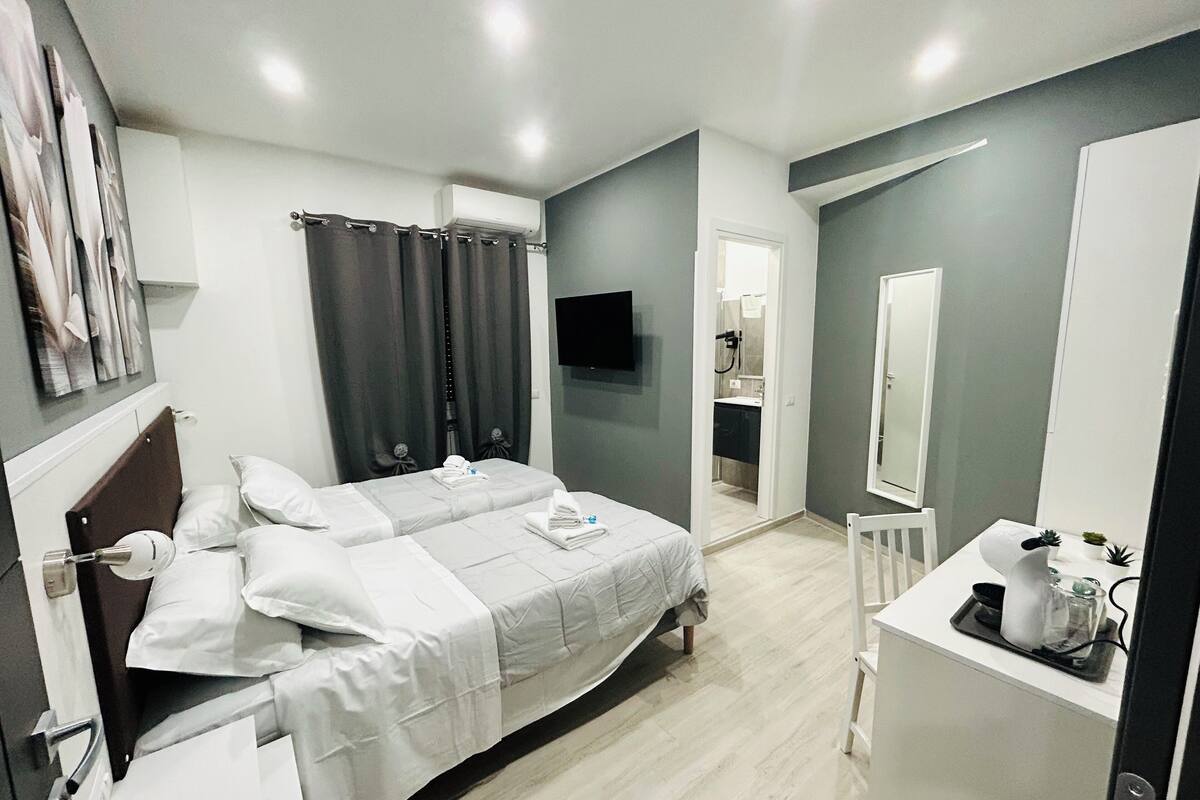 A modern bedroom with a bed, a vanity with a mirror, and a shower area.