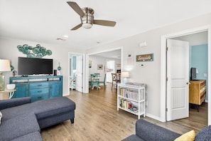 A living room with a sofa, a TV, a ceiling fan, and a bookshelf. - The Blue Pearl ~ PRIVATE POOL in the heart of Port A! & Detached Game Room! (Port Aransas)