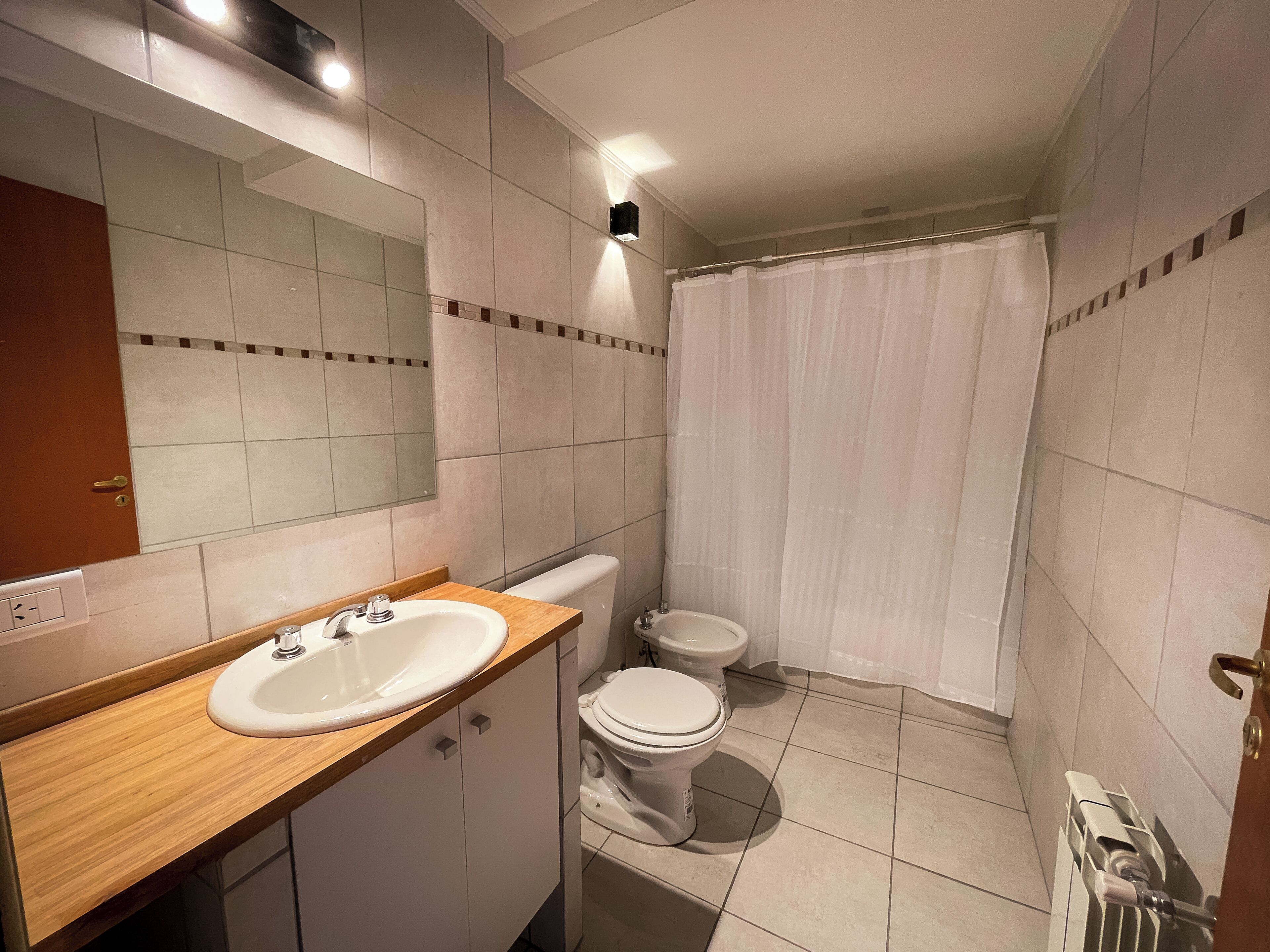A bathroom with a wooden vanity, a white sink, a toilet, and a shower curtain.