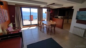 Amplia sala de estar con mesa y sillas de comedor, sofá y vistas al mar a través de amplios ventanales.