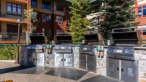 Ein Grillbereich mit vier Gasgrills, Steinpfeilern und einem gepflasterten Weg.