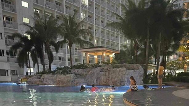 A pool area with lounge chairs, palm trees, and a building in the background. - Cozy-Stylish 1BR CONDO (Pasay)