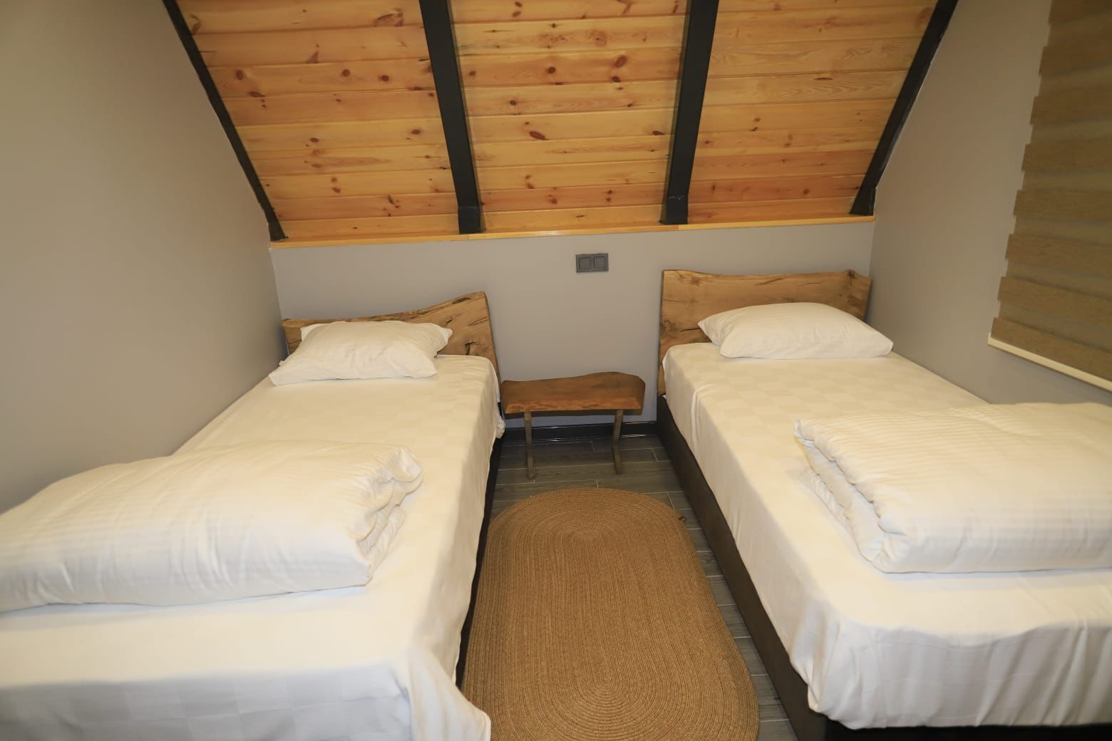 Une petite pièce agréable et chaleureuse, avec deux lits simples, un banc et un plafond en bois.