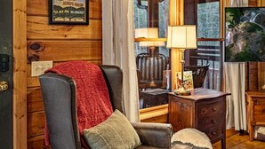 A cozy cabin interior with a leather armchair, a table with a lamp, and a framed sign advertising Atlanta Peach Farm.