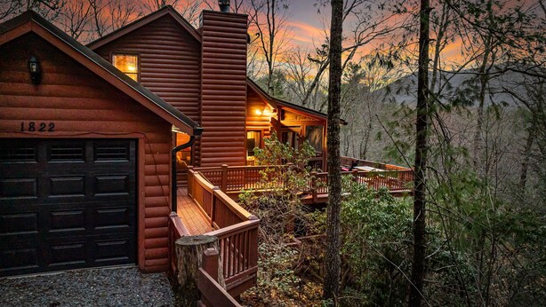 A log cabin with a garage, a deck, and a view of the surrounding forest.