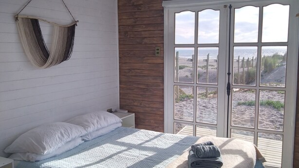 Une chambre avec un lit, un hamac suspendu, une vue sur la plage à travers une porte vitrée et des murs en bois.