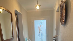 Un couloir avec un miroir encadré en bois, un radiateur, une table sur laquelle se trouve un vase, et une assiette décorative accrochée au mur.
