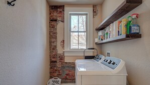 Une buanderie avec un mur en briques, une fenêtre, une étagère contenant des produits de nettoyage et un lave-linge.