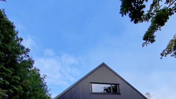 Un bâtiment moderne doté d’un toit triangulaire, entouré d’une végétation luxuriante et d’un jardin bien entretenu.