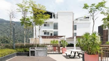 A modern multi-story building with a flat roof terrace, outdoor seating, and potted plants.