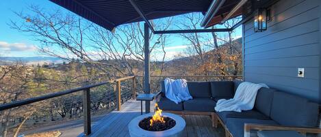 A covered deck with a fire pit, seating area, and a view of the landscape.