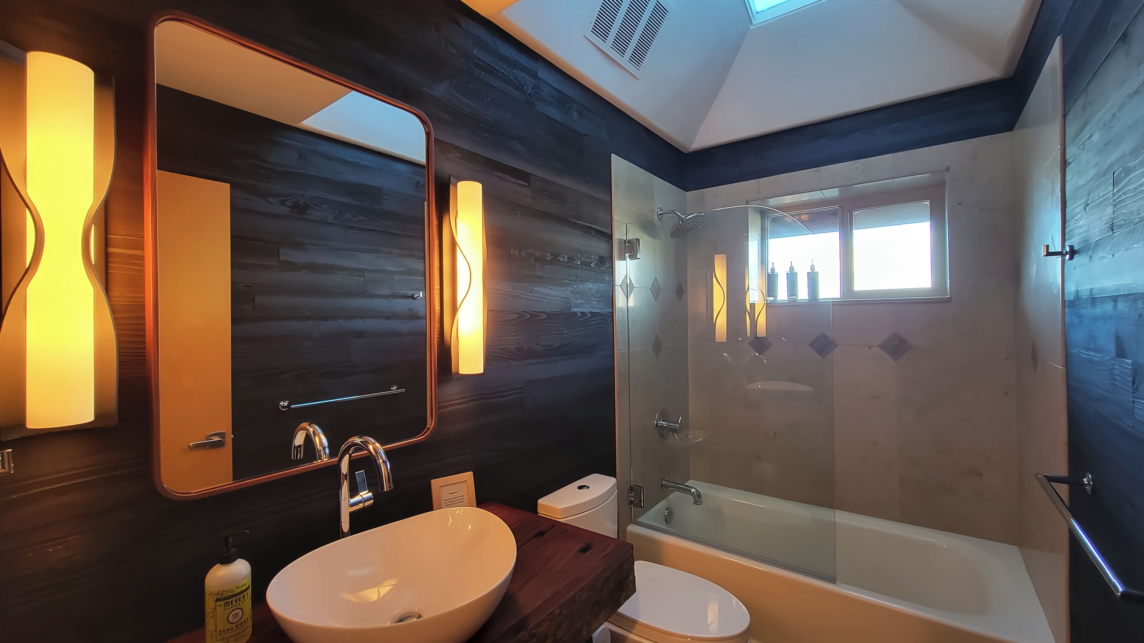 Un baño moderno con un espejo grande, un lavamanos, un inodoro y una ducha con mampara de vidrio.