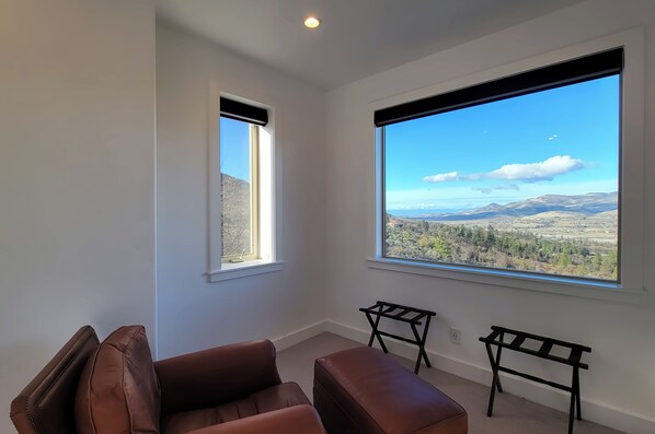 Habitación con un amplio ventanal que ofrece vistas a un paisaje montañoso. Hay dos sillas negras y una pequeña mesa.