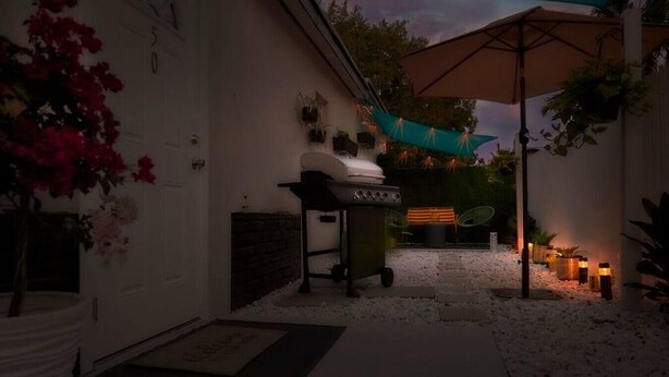 Patio trasero con una parrilla, mobiliario exterior e iluminación decorativa.