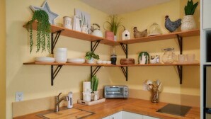 Una cocina con mostradores de madera, horno empotrado y estantes con utensilios de cocina y plantas.