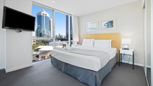 A hotel room with a large bed, a TV mounted on the wall, and a city view through the window. - Pool and Ocean Views at the H-Residences (Surfers Paradise)