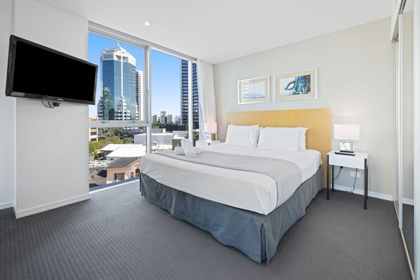 A hotel room with a large bed, a TV mounted on the wall, and a city view through the window. - Pool and Ocean Views at the H-Residences (Surfers Paradise)