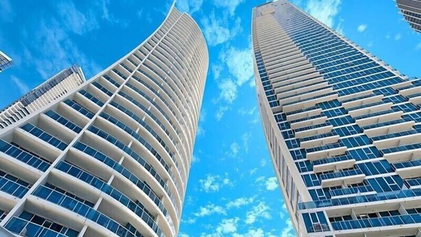 Two high-rise buildings with a curved facade and a clear blue sky in the background. - Pool and Ocean Views at the H-Residences (Surfers Paradise)