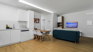 Et moderne køkken med hvide skabe, et spisebord med stole, en turkis sofa og et fladskærms-tv på væggen.
