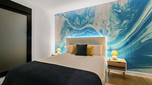 Et hotelværelse med en stor seng, to sengeborde med lamper og et vægmaleri.
