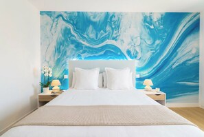 Une chambre à coucher avec un grand lit, du linge de lit blanc, deux tables de chevet avec des lampes et une fresque murale.