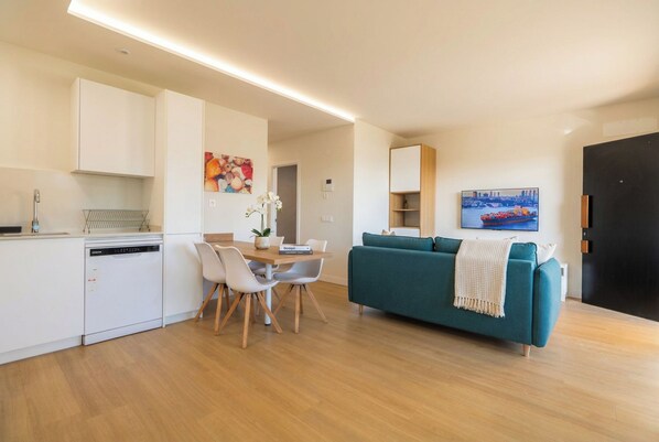 Une cuisine moderne avec des meubles blancs, une table à manger avec des chaises, un canapé de couleur turquoise et un tableau au mur.