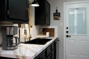 A kitchen with dark cabinets, a white countertop, a coffee maker, and a window with blinds.
