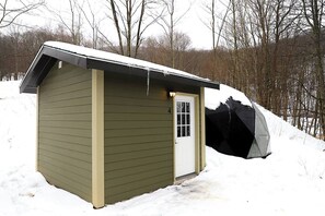 A small, single-story shed with a white door and a window, surrounded by snow and trees. - Glamping Dome #4 in Snowshoe, Wv (Snowshoe)