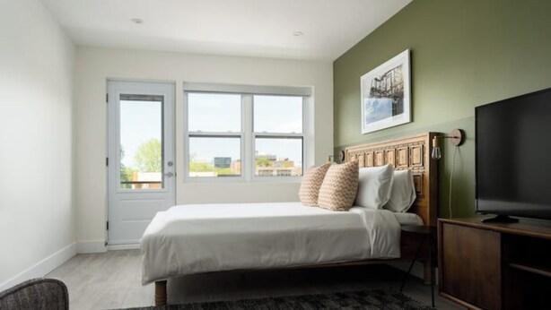 A bedroom with a bed, a television, a large window, and a door. - Stunning Modern Loft in the heart of Le Plateau (Montréal)