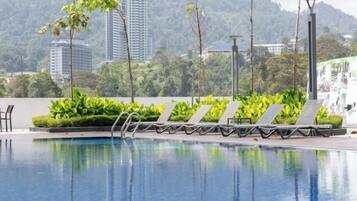 A swimming pool with lounge chairs and a view of a cityscape with buildings and greenery.