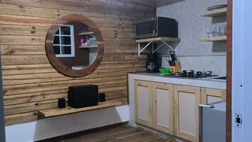 Una cocina con paneles de madera, un espejo redondo, un microondas, una estufa a gas y una cafetera.