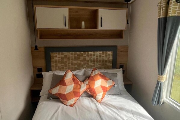 Un lit avec deux coussins aux motifs géométriques, une tête de lit en bois et une étagère intégrée au-dessus du lit.