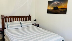 Un lit avec une couvre-lit à rayures, une lampe de chevet et un tableau représentant un paysage, accroché au mur.