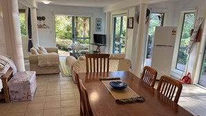 Un coin repas avec une table et des chaises en bois, un téléviseur posé sur un meuble et un réfrigérateur.