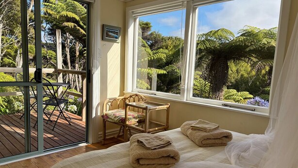 Une chambre avec une grande fenêtre, un lit avec des serviettes, une chaise et une vue sur la verdure à l’extérieur.