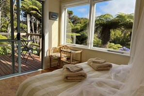 Ein Schlafzimmer mit großem Fenster, einem Bett mit Handtüchern, einem Sessel und Blick auf Grünfläche.