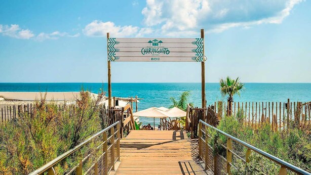 Un muelle de madera que conduce a una playa, con un letrero que dice "CHIRINGUE".