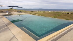 A clear swimming pool with a view of distant hills and a clear sky. - Hilltop Vineyard Estate | Infinity Pool + Views (Paso Robles)