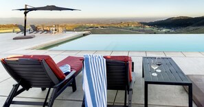 Un área de piscina al aire libre con sillones de descanso, una mesa con vasos y vistas a colinas distantes.