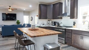 A modern kitchen with dark cabinets, a wooden island, bar stools, a stainless steel trash can, and a coffee maker. - Luxury 7BR Equestrian Estate Farmhouse Near Tryon Equestrian Center/Lake Lure (Mill Spring)
